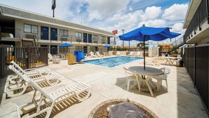 Un espace piscine d’hôtel avec des chaises longues, une table et des parasols.