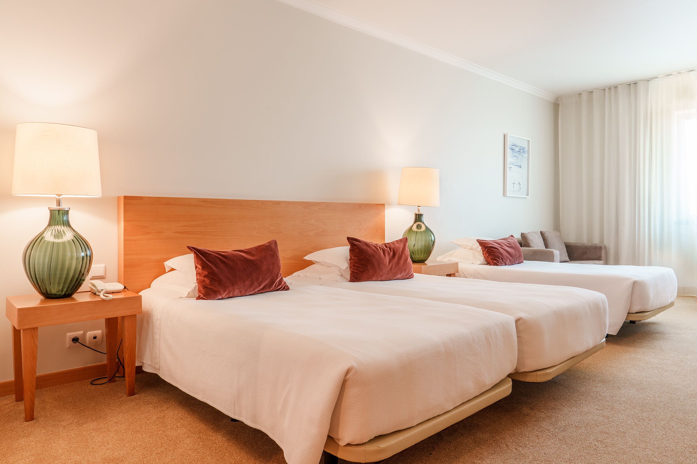 A hotel room with two beds, a nightstand with a lamp, a telephone, and a painting on the wall.