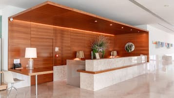 Una recepción con un panel de madera de fondo, un mostrador de mármol y una planta en maceta.