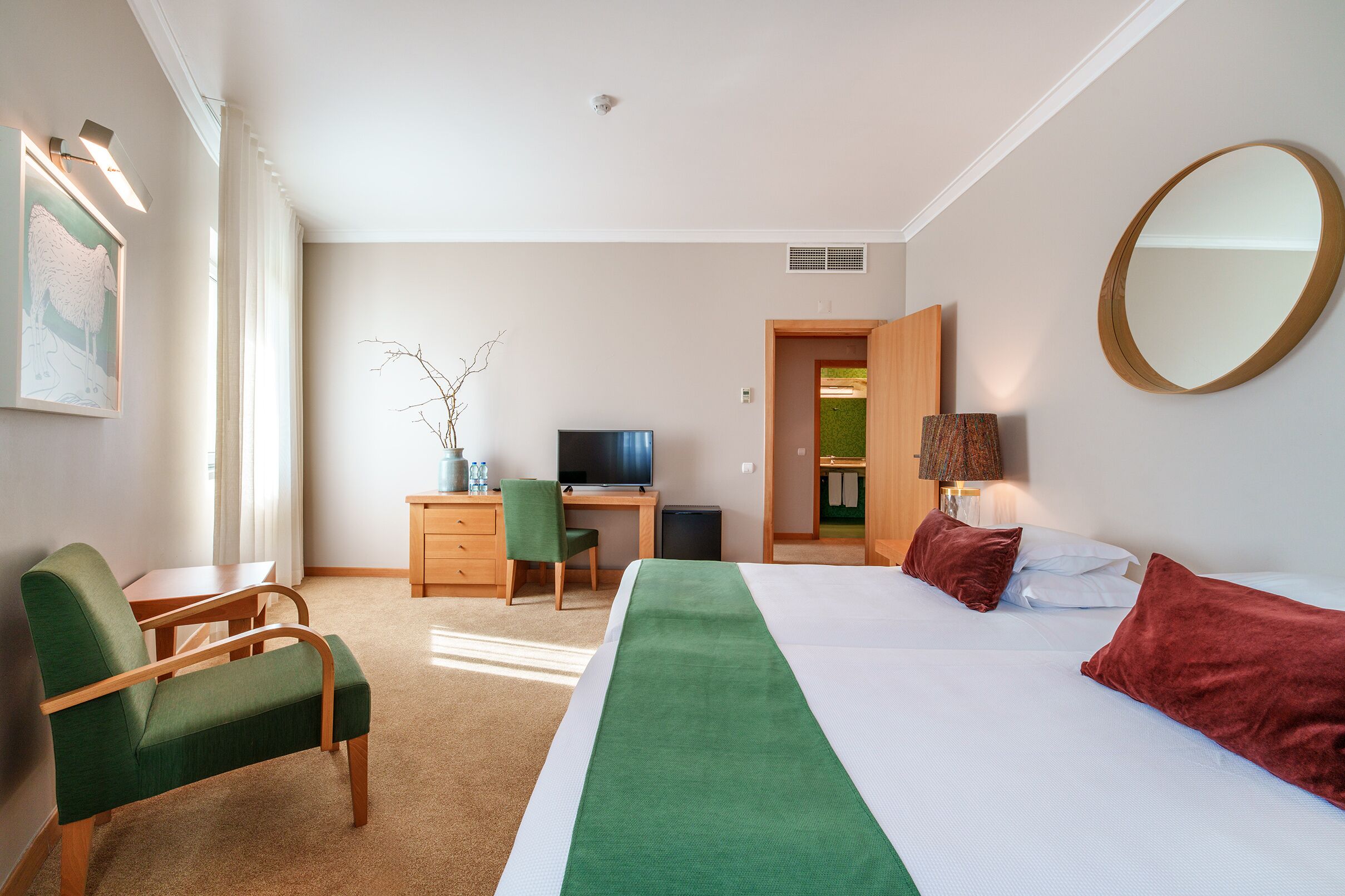 A hotel room with a bed, a desk, a chair, a television, and a mirror.