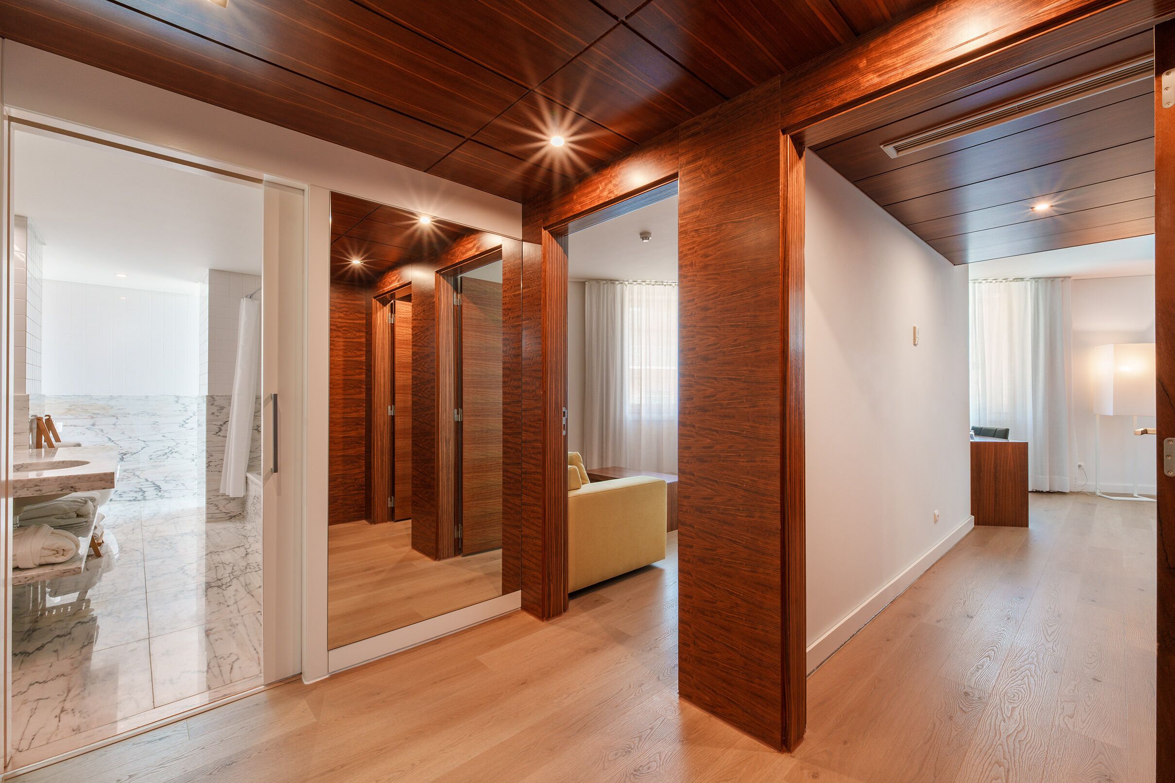 A modern interior with a wooden ceiling, a bathroom with a marble vanity, and a living area with a sofa.