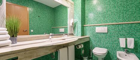 A bathroom with a green mosaic tile wall, a marble sink, a toilet, a bidet, and a towel rack.