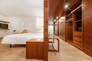 Un dormitorio moderno con cama, mesita de noche, armario de madera y televisor en la pared.