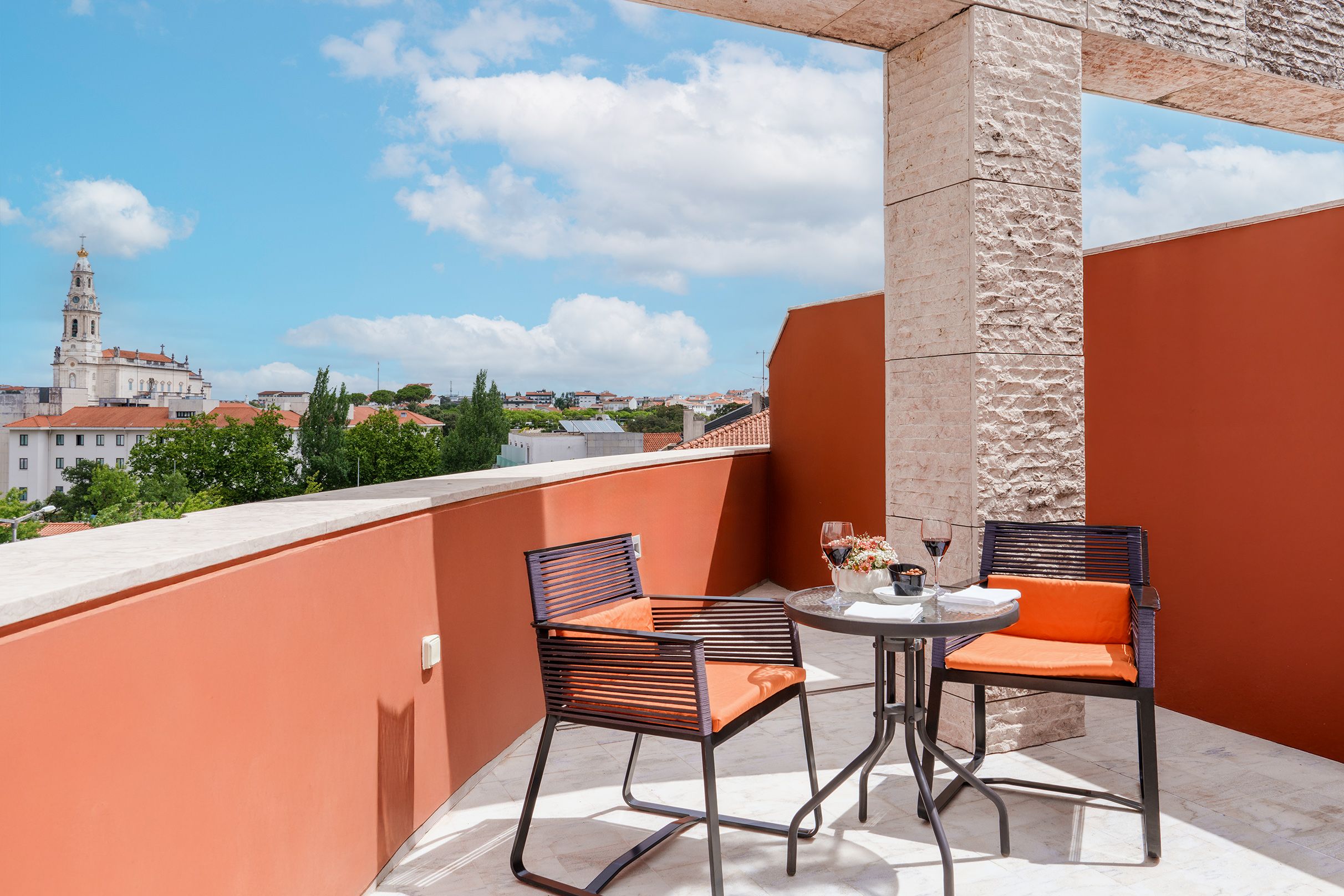 A balcony with two chairs and a table, overlooking a cityscape with a prominent church tower.