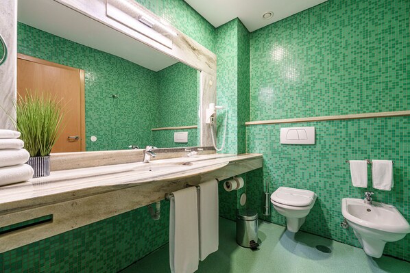 Un baño con pared de mosaico verde, lavamanos de mármol, inodoro, bidé y un perchero para toallas.