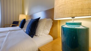 Habitación de hotel con dos camas, cabecera de madera, una lámpara azul y una silla.