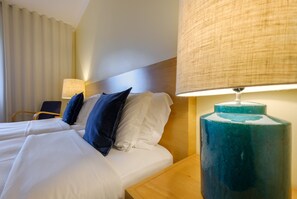 Camera d'albergo con due letti, una testiera in legno, una lampada blu e una sedia.
