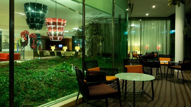 Un espacio interior moderno con paredes de vidrio, una zona ajardinada y muebles contemporáneos.