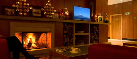 Una hall accogliente con camino, televisione che mostra una vista sulle montagne e reception.