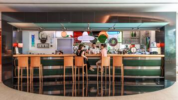 Una zona de bar con taburetes, una barra y diferentes botellas y vasos.