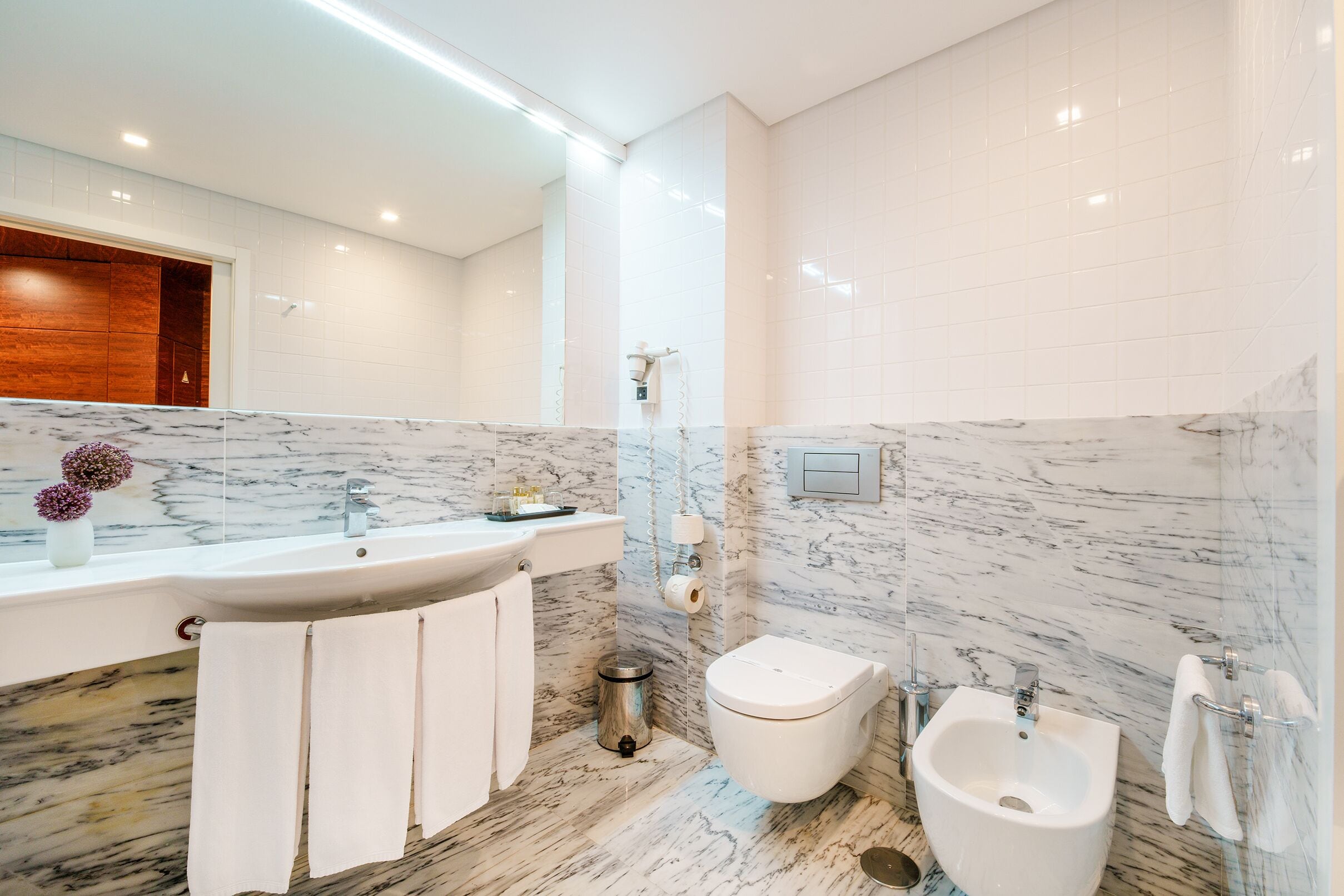 A modern bathroom with a marble sink, a bidet, and a bidet with a handheld showerhead.
