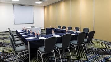 A conference room with a projector screen, tables with water bottles, and chairs.