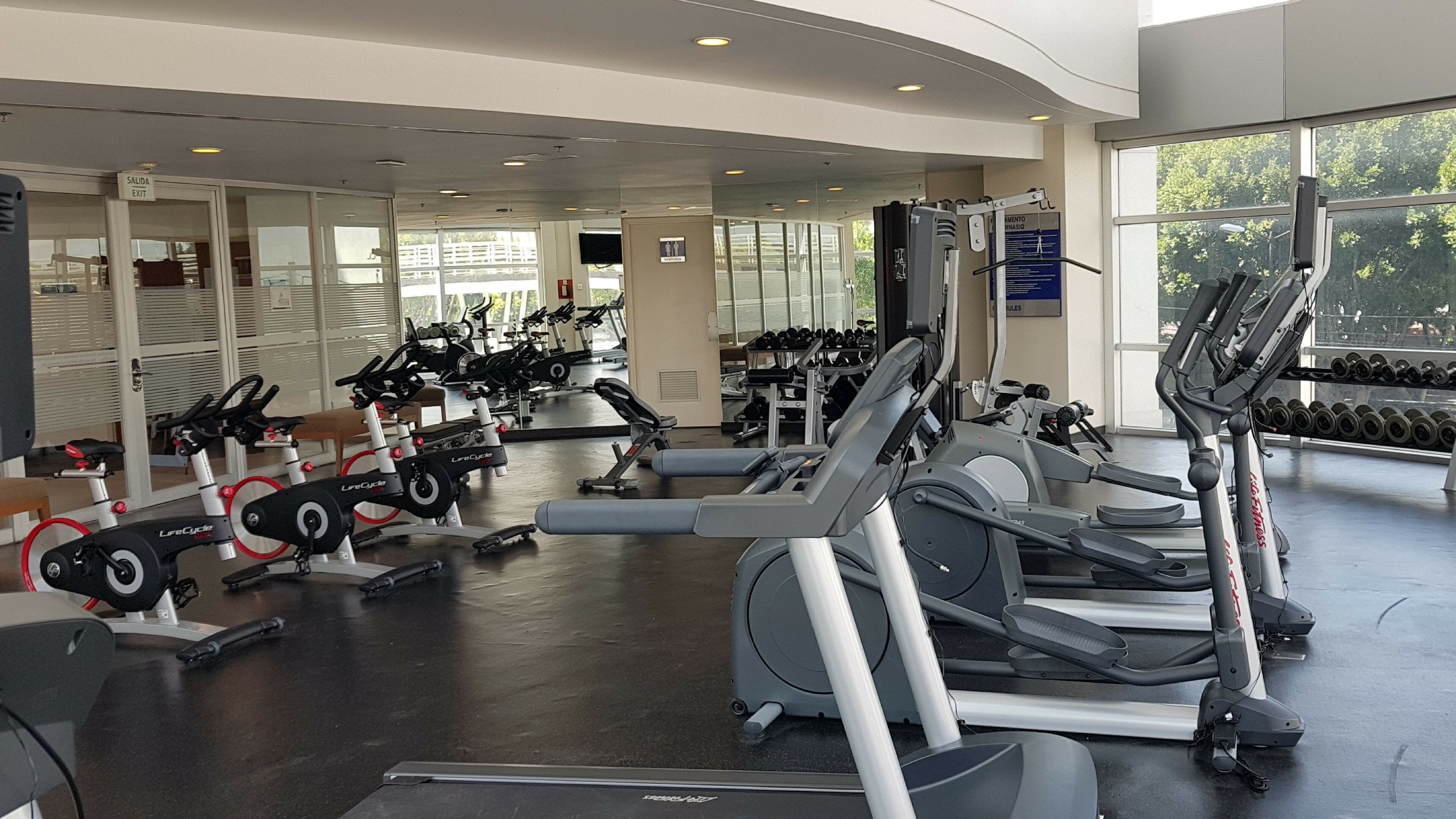 Un gimnasio con equipo de ejercicio variado, incluyendo cintas de correr, bicicletas estáticas y máquinas de pesas.
