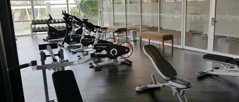 Une salle de sport équipée de divers appareils d’exercice, notamment des tapis de course et des appareils de musculation, ainsi que d’un banc.