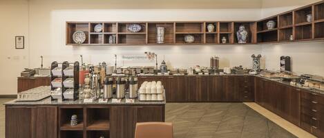 Un área de desayuno buffet con una variedad de alimentos, una estación de café y jarrones decorativos en estantes.