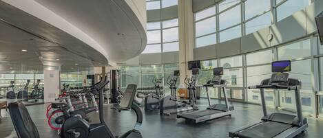 A modern gym with various cardio and strength training equipment, large windows, and a curved ceiling.