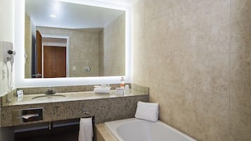 Une salle de bain moderne avec un comptoir en granit, un lavabo blanc, un grand miroir, un porte-serviettes et une baignoire.