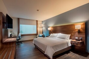A modern hotel room with a large bed, a desk, a chair, a TV, and a window.