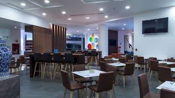 A modern dining area with multiple tables and chairs, a large decorative vase, and a colorful wall art piece.