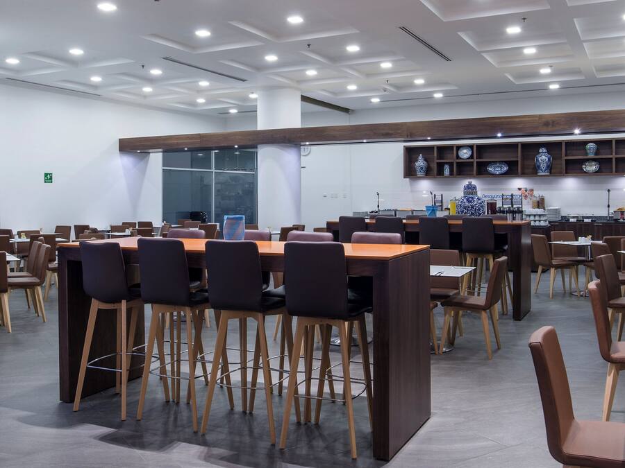 Un comedor moderno con varias mesas y sillas, una zona de cocina con platos decorativos, y un televisor de pantalla plana montado en la pared.
