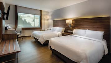 A hotel room with two beds, a desk, a chair, a TV, and a window.