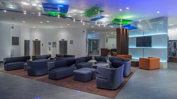 A modern lobby with seating areas, a reception desk, and a staircase leading to other floors.