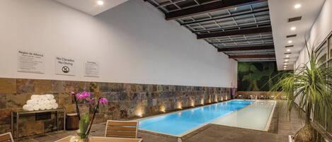 Piscina interna com parede de pedra, área de estar e placas com regras.