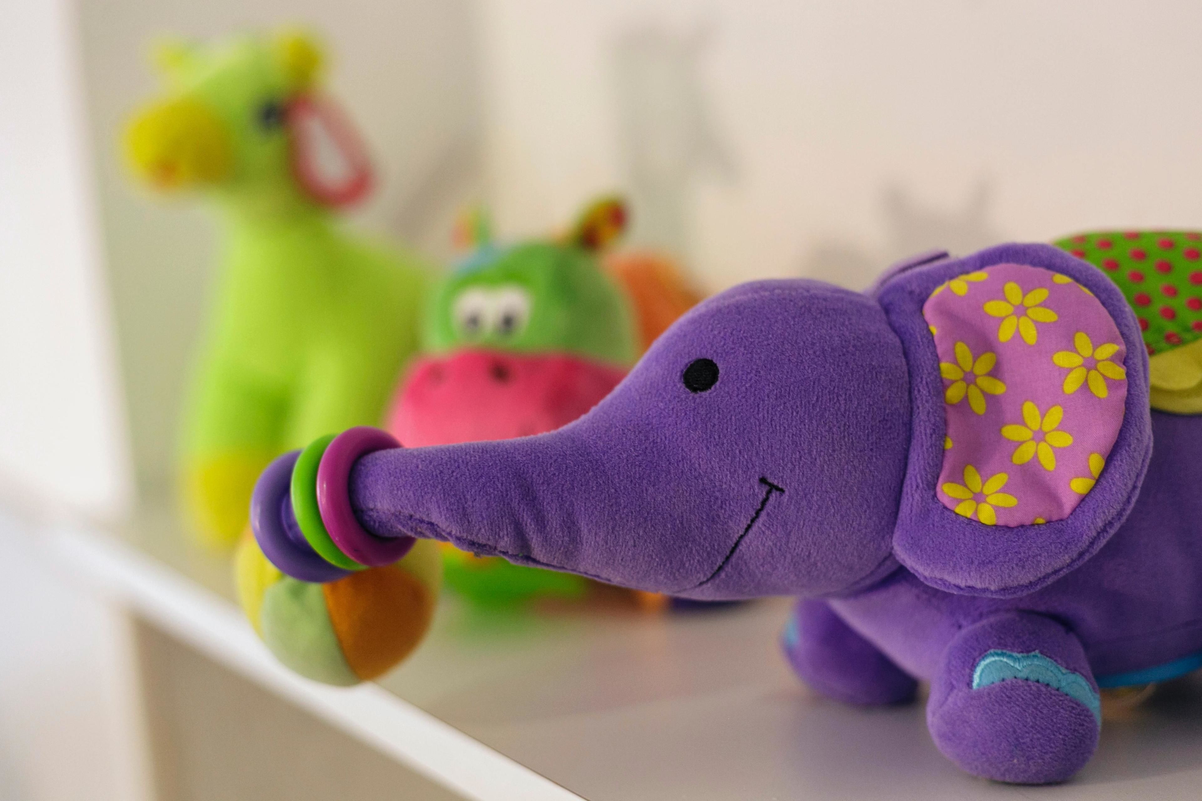 Un elefante di peluche con corpo viola e un motivo floreale rosa e giallo sull'orecchio.