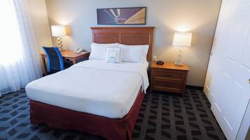 A hotel room with a large bed, two bedside tables with lamps, a wooden headboard, a painting above the bed, and a patterned carpet.
