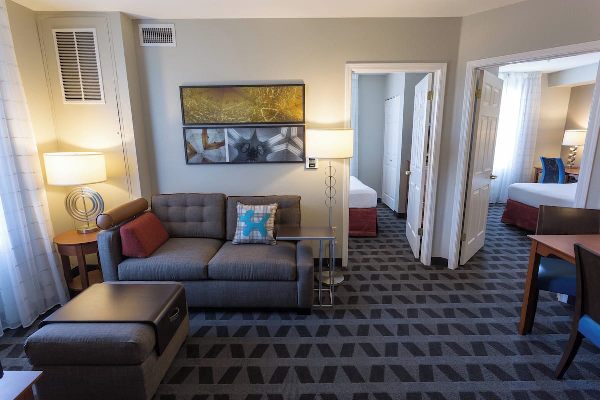 A hotel room with a sofa, a small table, a lamp, a bed, and a desk.