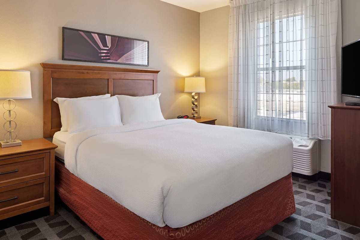 A hotel room with a large bed, two bedside tables, a TV, and a window with curtains.