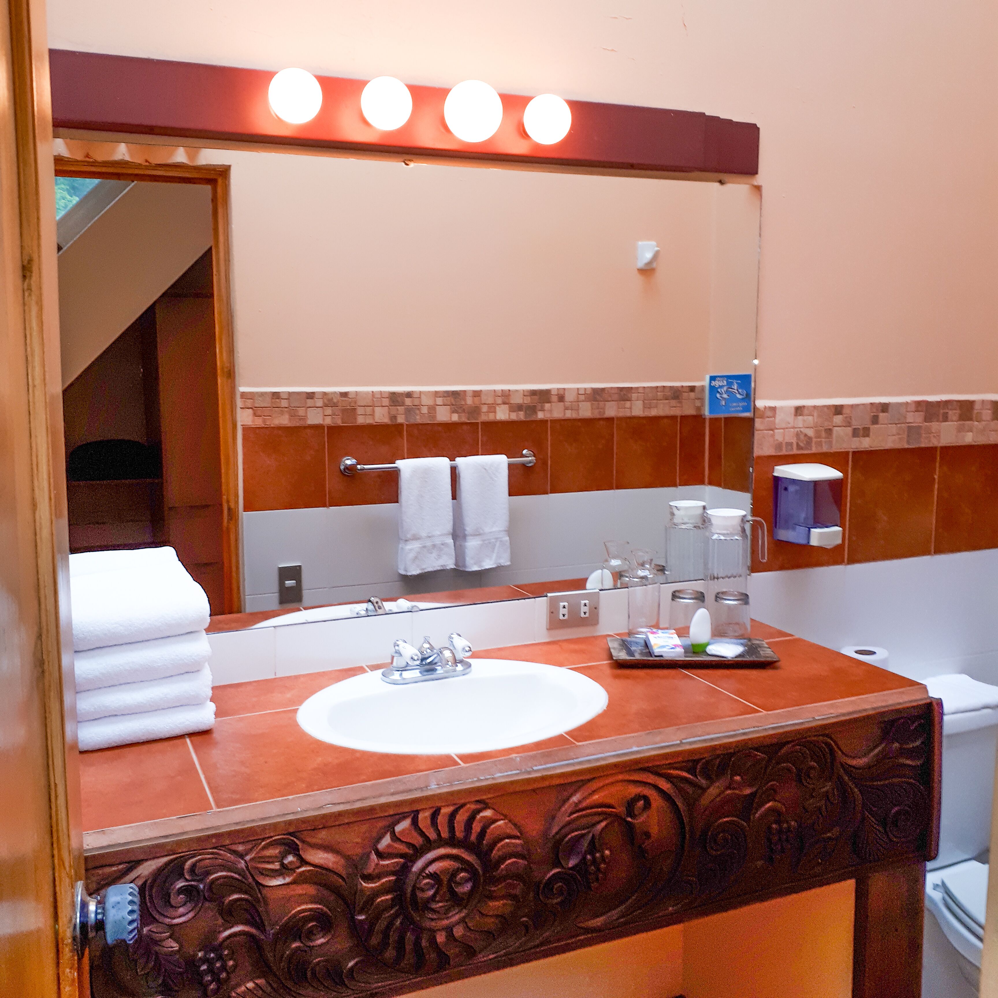 A bathroom with a vanity, sink, and mirror. There are towels stacked on the sink, a soap dispenser, and a toothbrush holder.