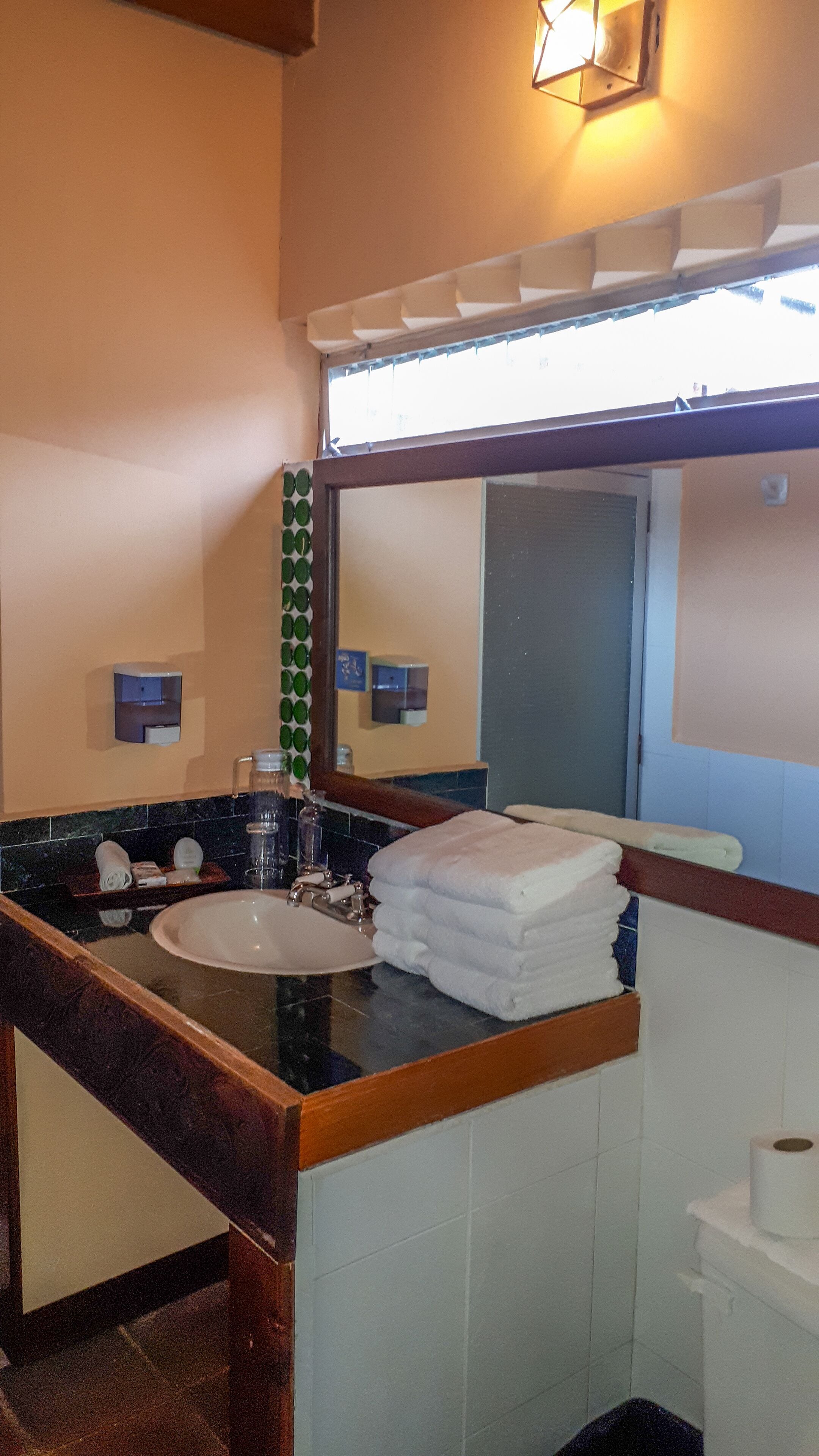 Un baño con lavamanos, espejo, toallero y ventana.