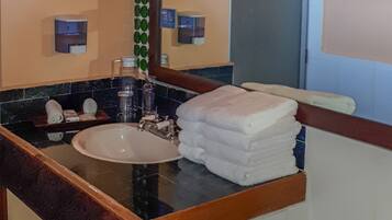 Un baño con lavamanos, espejo, toallero y ventana.