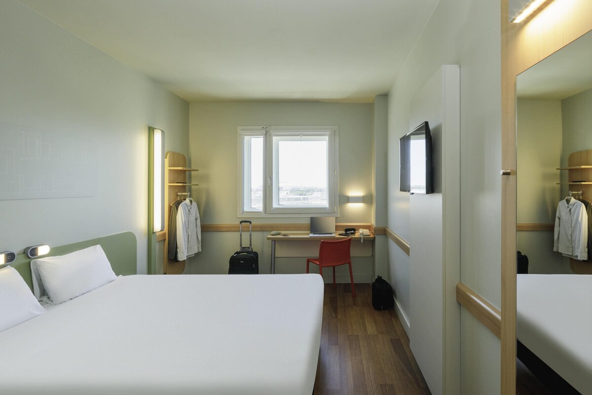Ett hotellrum med två sängar, ett skrivbord, en stol, ett fönster och en spegel.