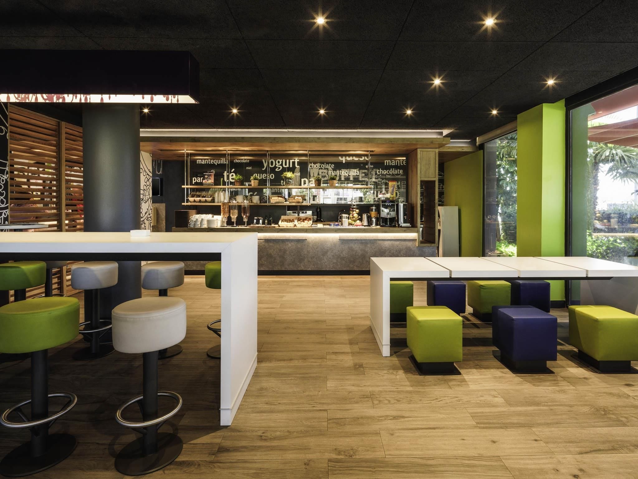 Un café moderno con barra, suelo de madera y asientos coloridos.