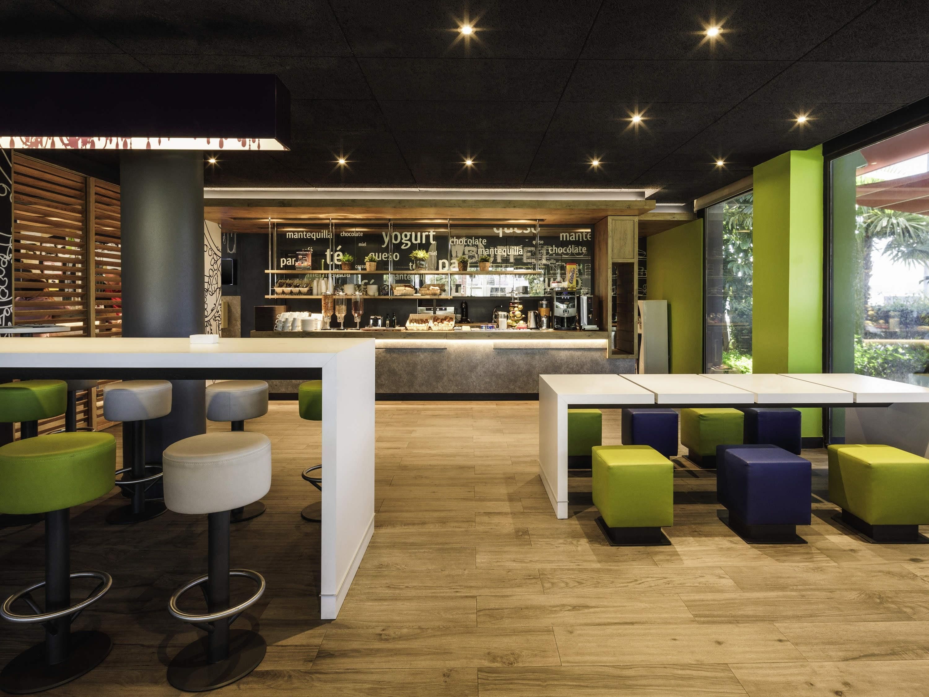 A modern bar area with wooden slats, a counter displaying various beverages, and seating with green and white stools.