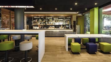 Zona de bar moderna amb lamel·les de fusta, barra que mostra diverses begudes i seients amb tamborets verd i blanc.
