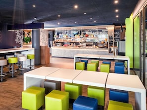 Interior moderno de café, com diversas áreas de estar, balcão com vários itens alimentícios e cozinha à vista.