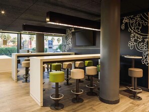 A modern bar area with high stools, a counter, and a large pillar. - ibis budget Malaga Aeropuerto Avenida Velazquez (Málaga)