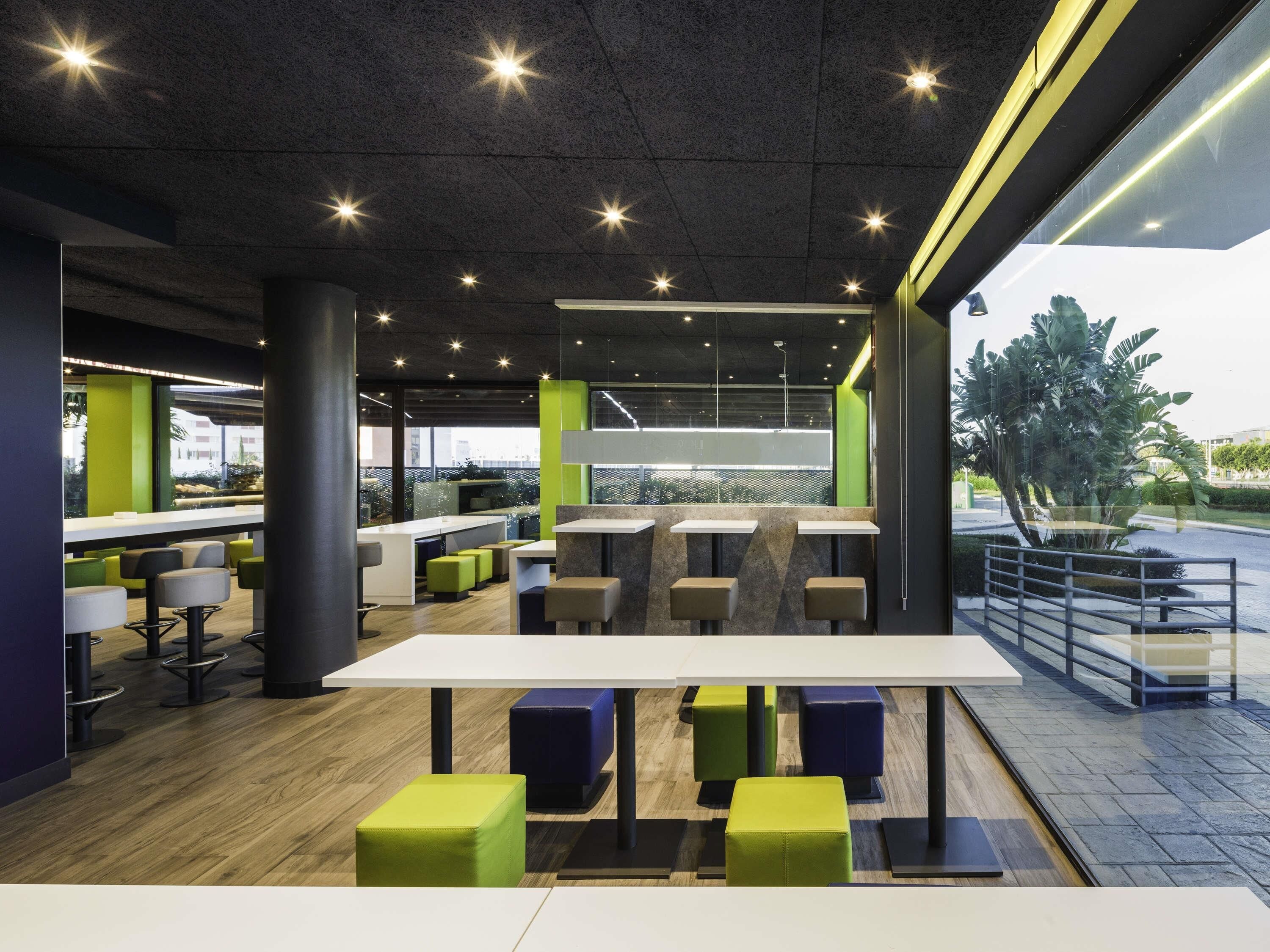 A modern indoor space with tables and chairs, a bar area, and a view through large windows.