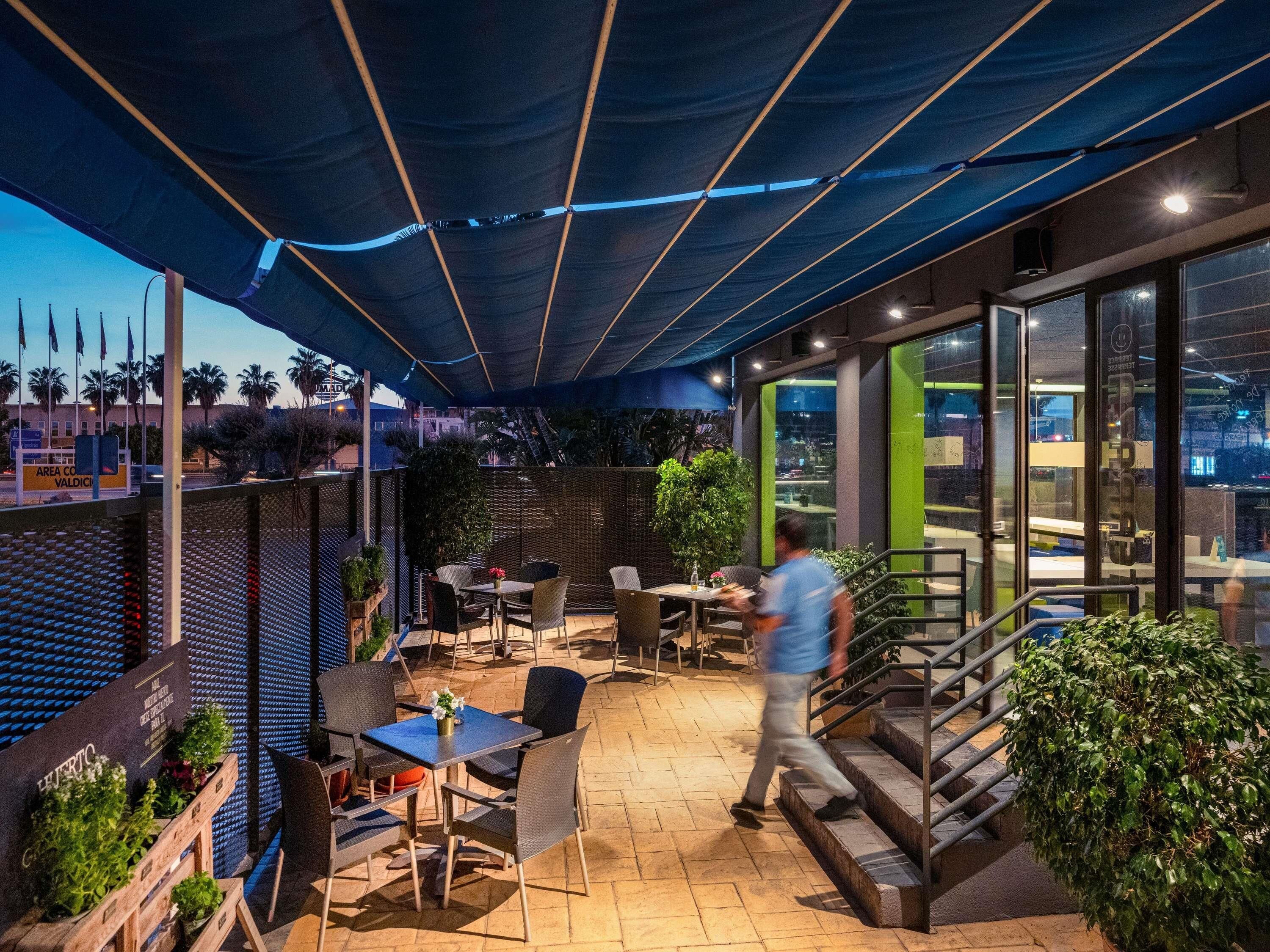Un patio al aire libre con mesas y sillas, una escalera y vistas a la ciudad.
