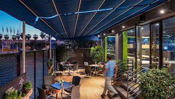 Un patio al aire libre con mesas y sillas, una escalera y vistas a la ciudad.