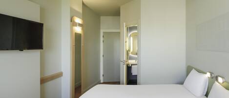 Habitación de hotel con cama, televisor montado en la pared y baño visible a través de una puerta abierta.