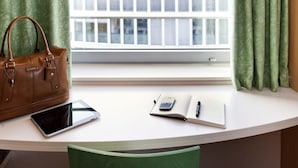 Una habitación con un escritorio blanco, un bolso de cuero marrón, una tableta, un cuaderno y un bolígrafo.