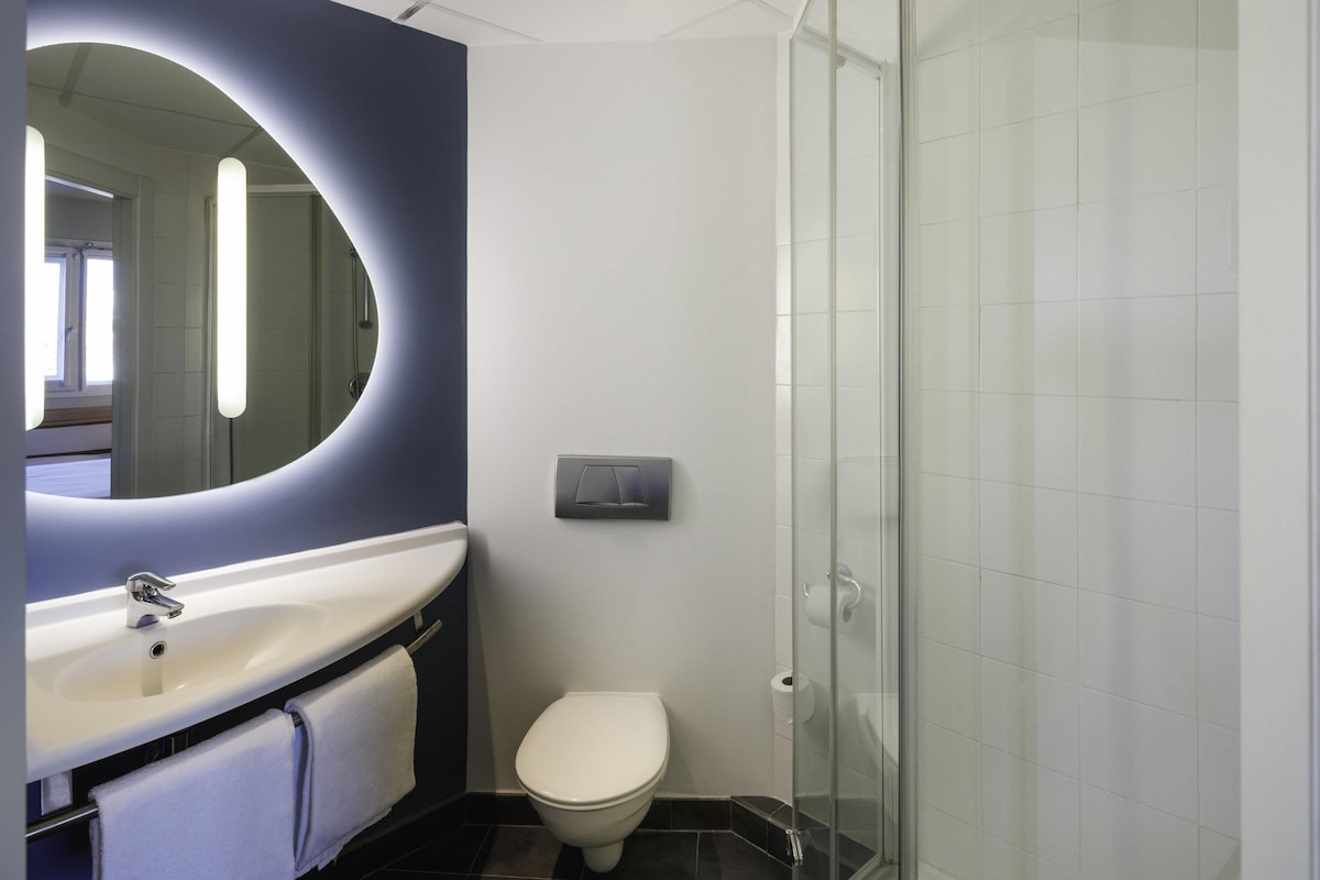 A modern bathroom with a white sink, a mirror, a toilet, and a glass shower enclosure.