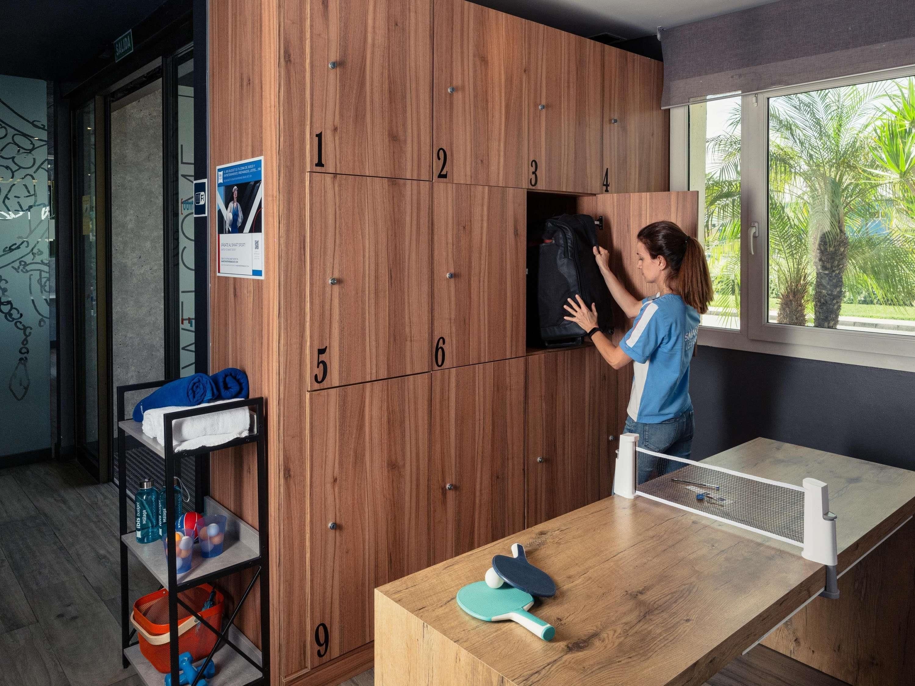 Una habitación con casilleros numerados, una mesa de ping pong y un ventanal con vista a palmeras.