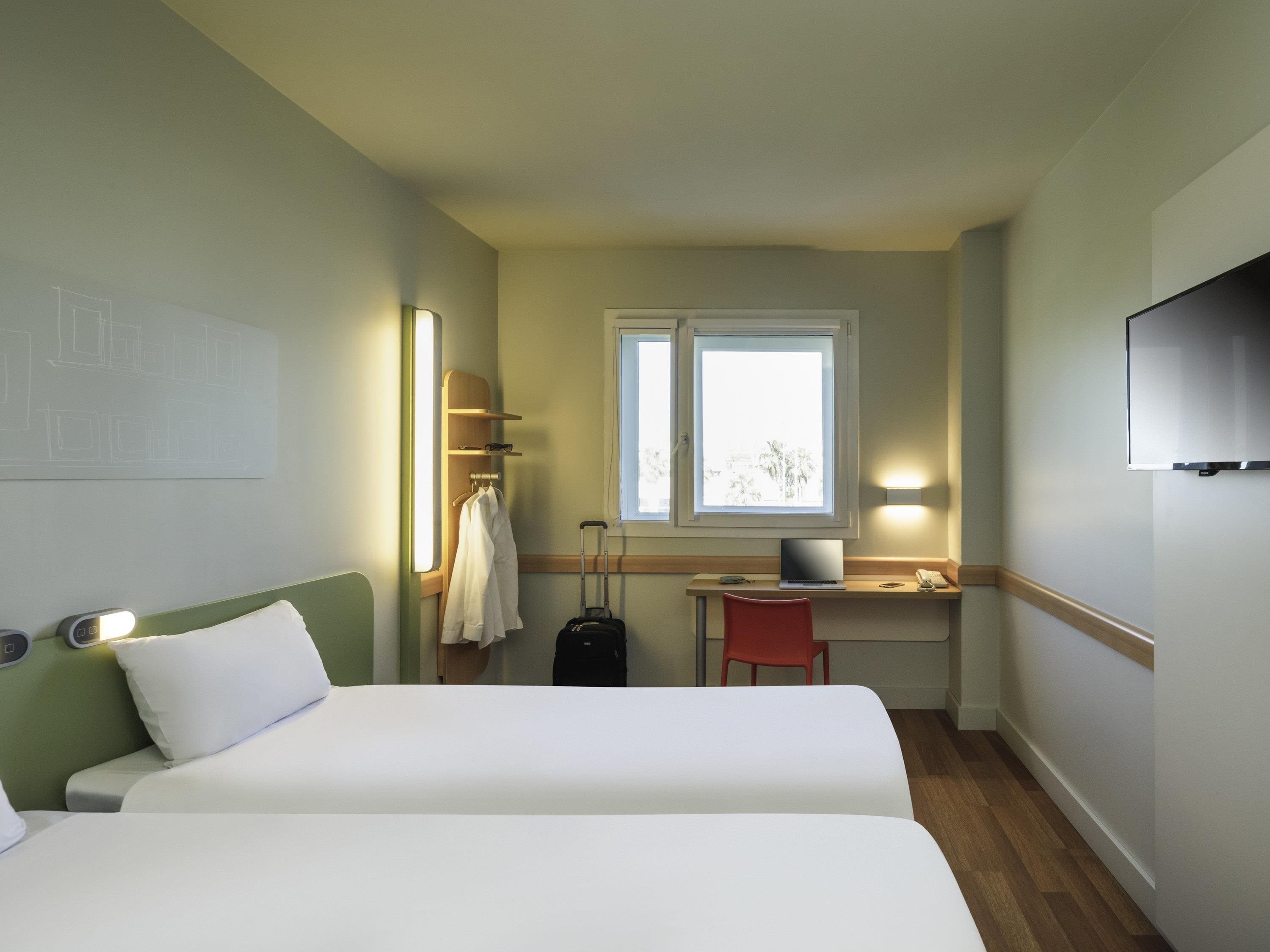 Una habitación de hotel con dos camas, un escritorio, una silla, un televisor y una ventana.