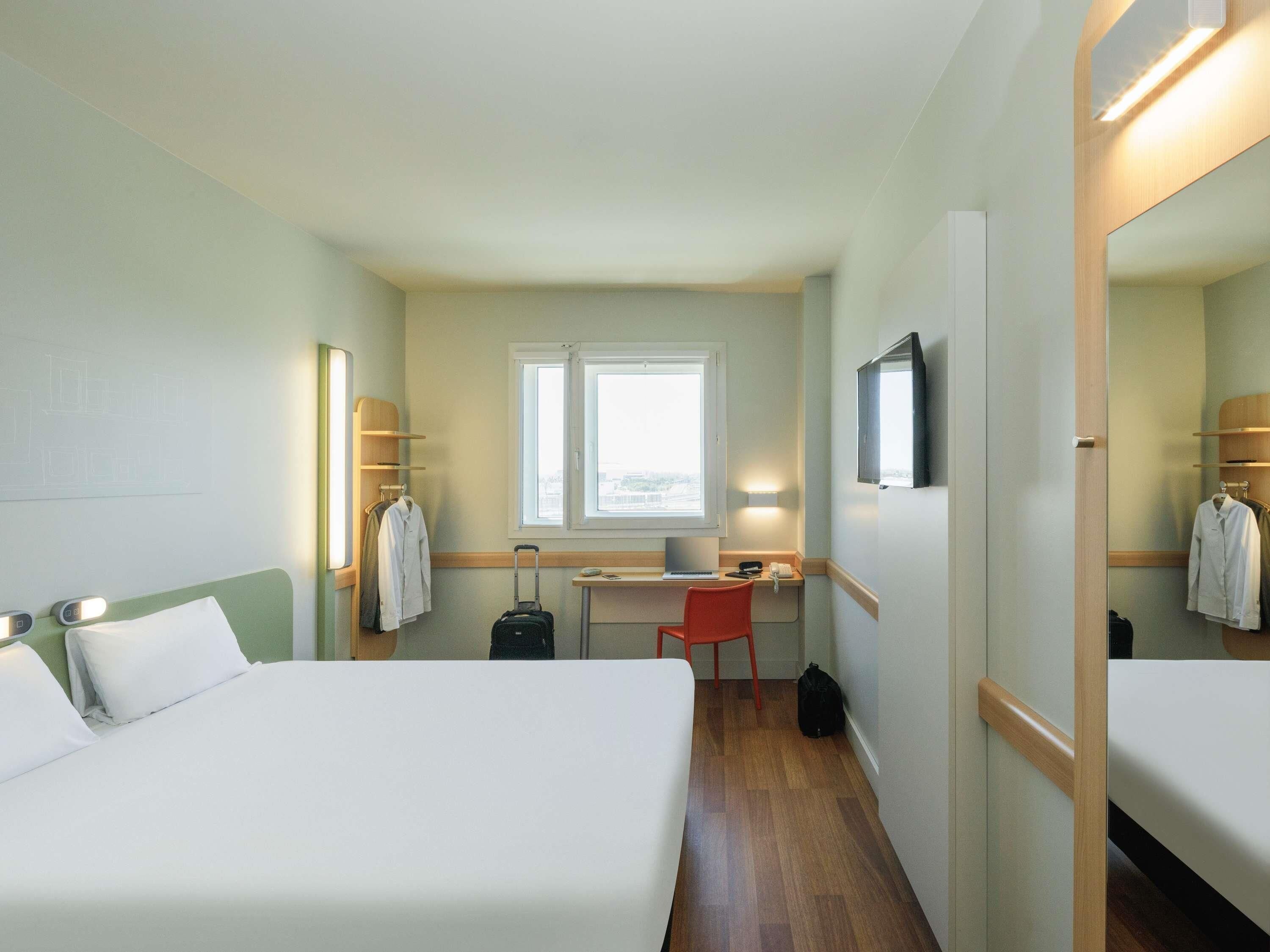 A hotel room with two beds, a desk, a chair, a suitcase, and a TV.