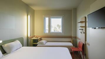 Une chambre d’hôtel avec un grand lit, un lit plus petit, un bureau avec un téléphone, une chaise, une fenêtre et un téléviseur fixé au mur.